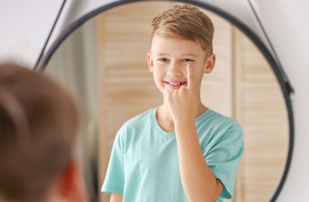 Smiling young boy standing at a mirror putting in contact lenses.